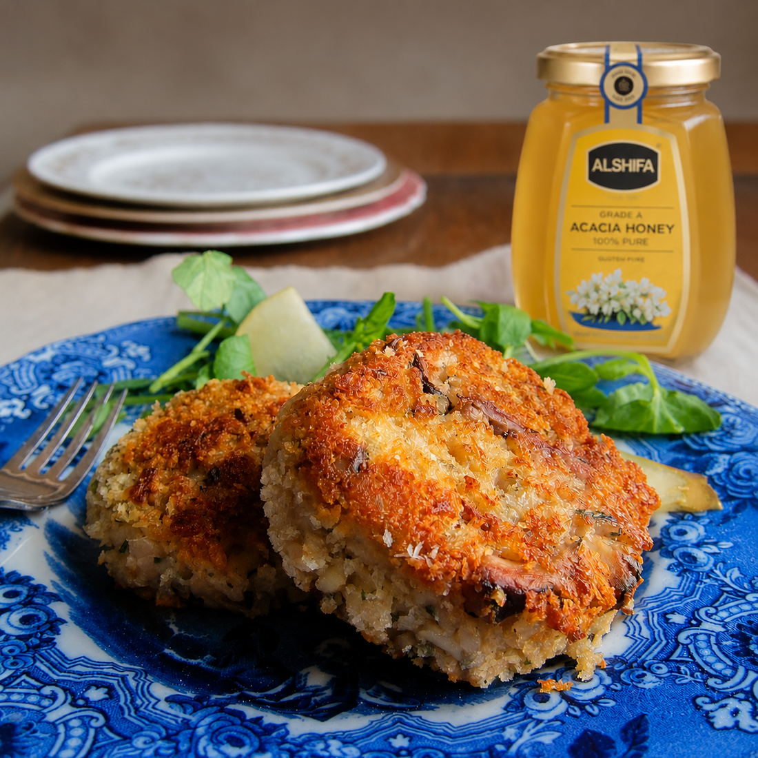 Golden porcini saffron risotto cakes on a blue plate beside a jar of ALSHIFA Acacia Honey