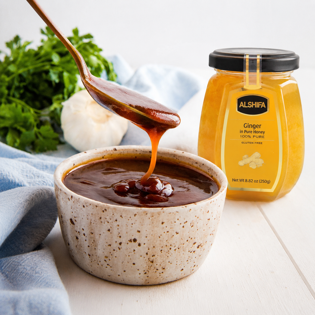 Spoonful of glossy honey BBQ sauce over a bowl beside a jar of ALSHIFA Ginger in Pure Honey
