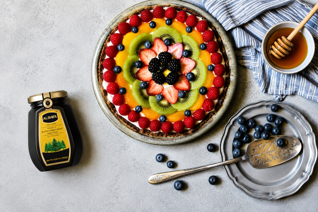 Frozen yogurt pie topped with fresh berries, kiwi, and orange beside a jar of ALSHIFA Black Forest Honey