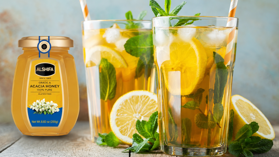 Two glasses of iced tea with lemon and mint beside a jar of ALSHIFA Acacia Honey